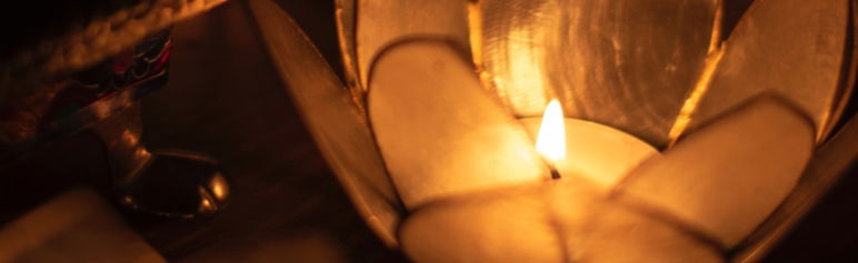 close up image of lotus flower candle holder with lit tea light candle on a dark background