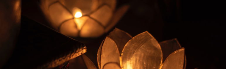 close up of lit candle in lotus flower candle holder agains a dark background